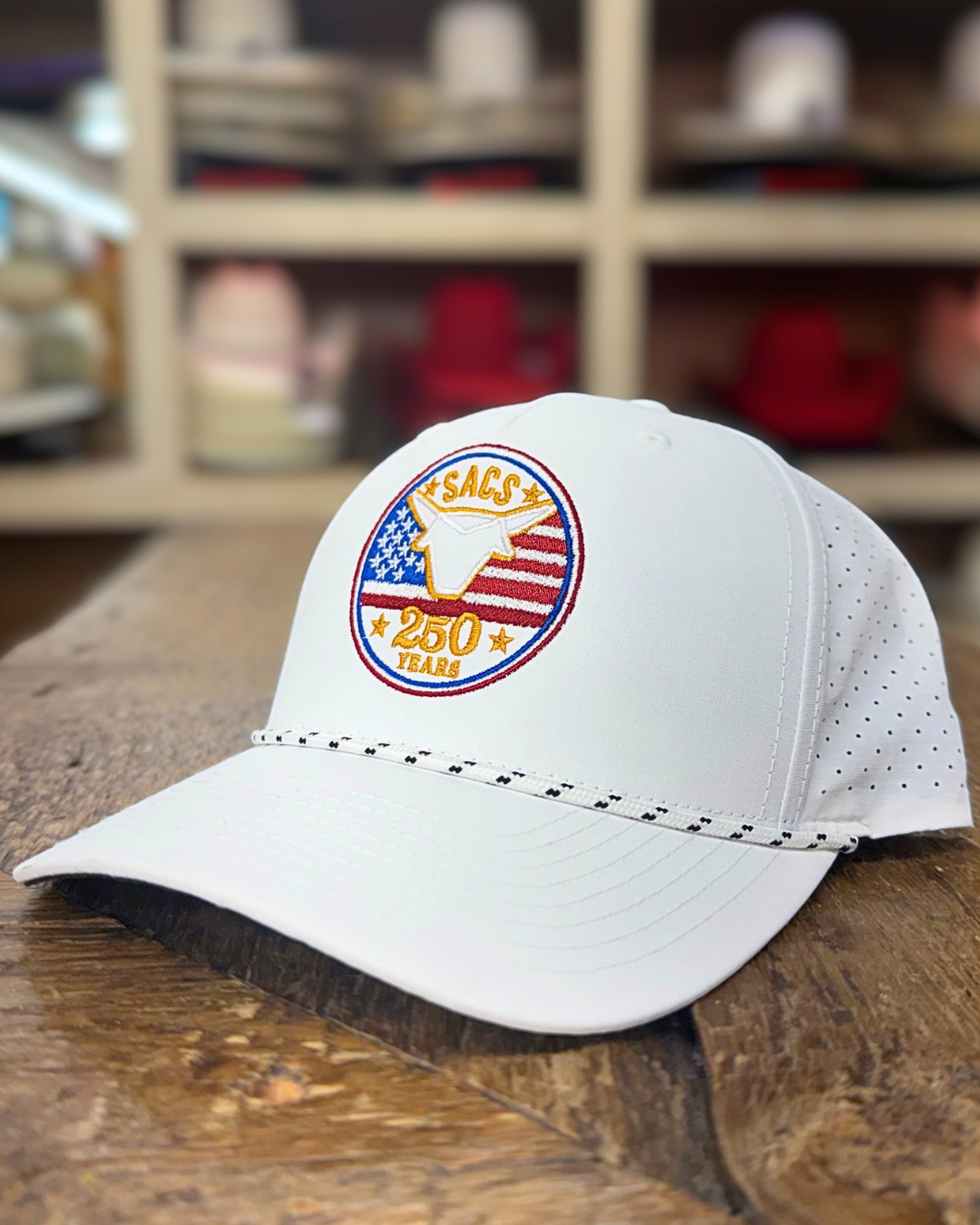 White cap with a logo on a wooden surface, with shelves of caps in the background.