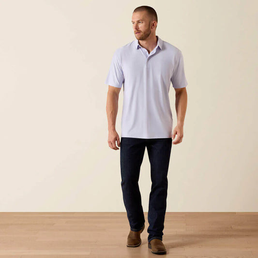 Man wearing a light blue polo shirt and dark jeans standing against a plain background
