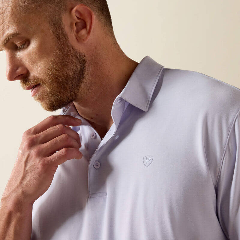 Man wearing a light purple polo shirt with a logo on a beige background
