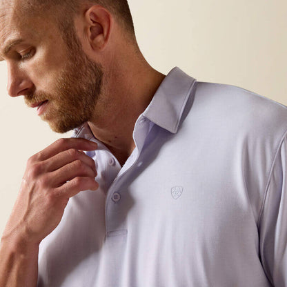 Man wearing a light purple polo shirt with a logo on a beige background