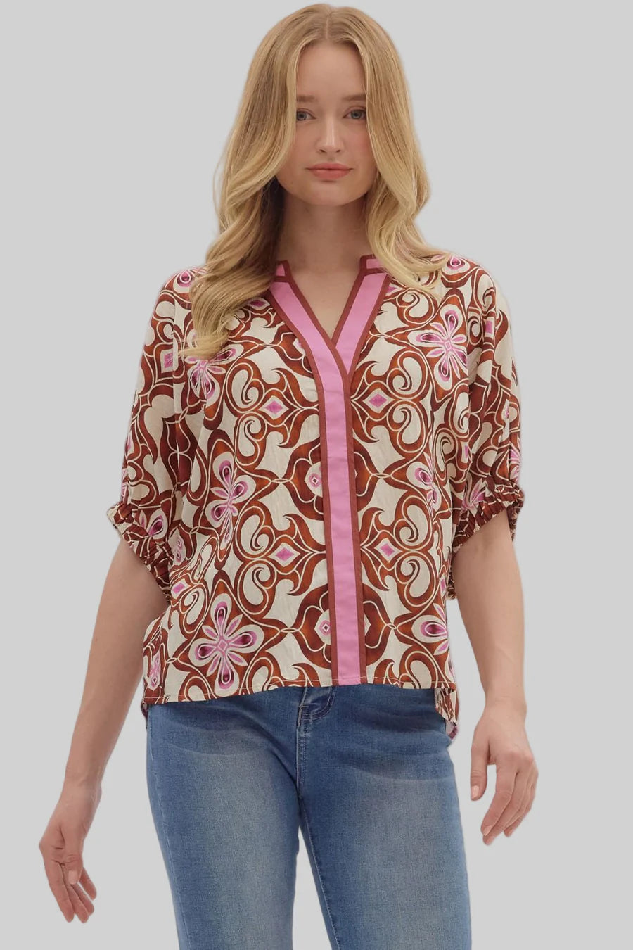Woman wearing a patterned blouse with pink accents and blue jeans on a white background