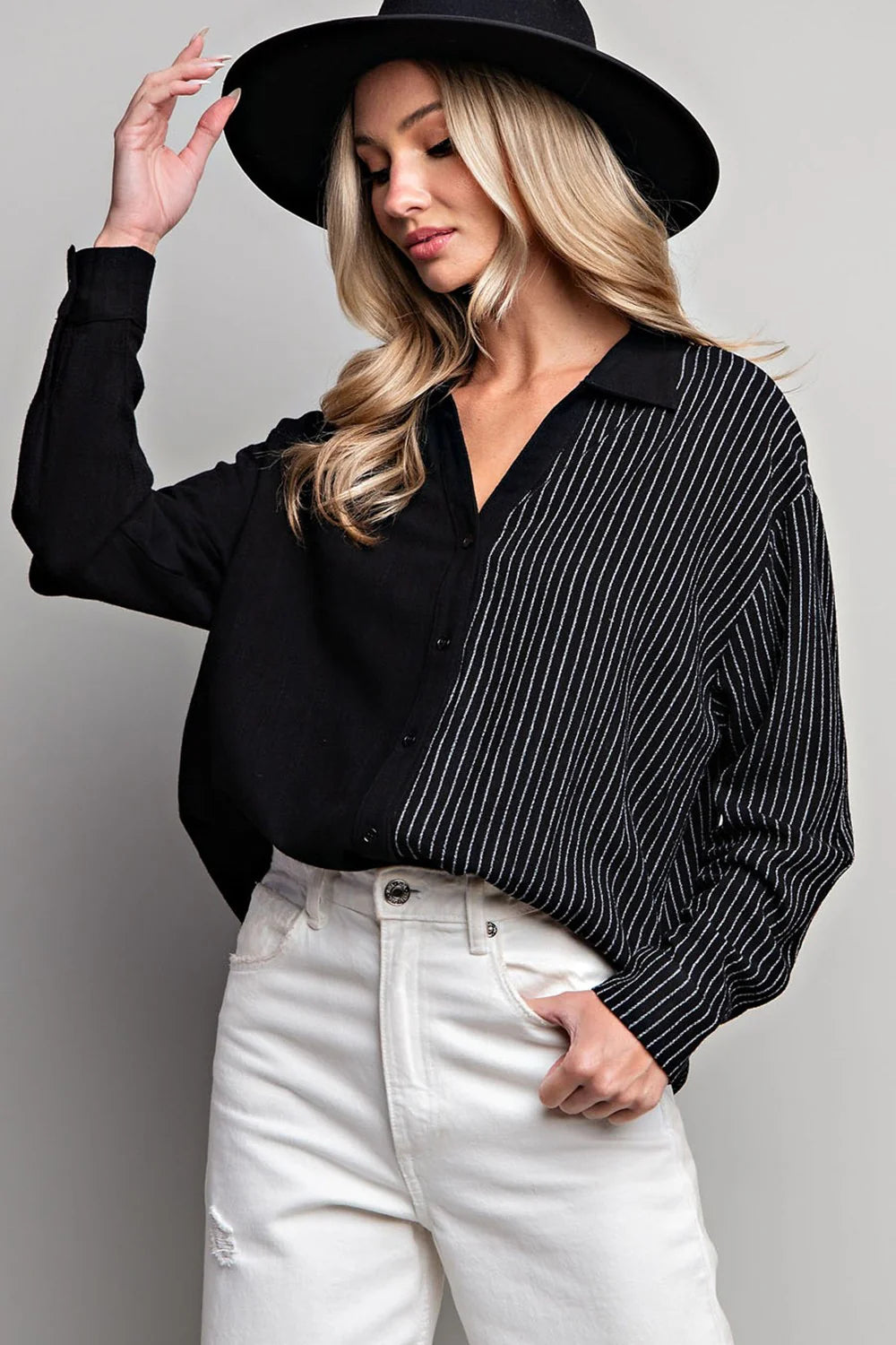 Woman wearing a black hat, black shirt, and white pants against a gray background