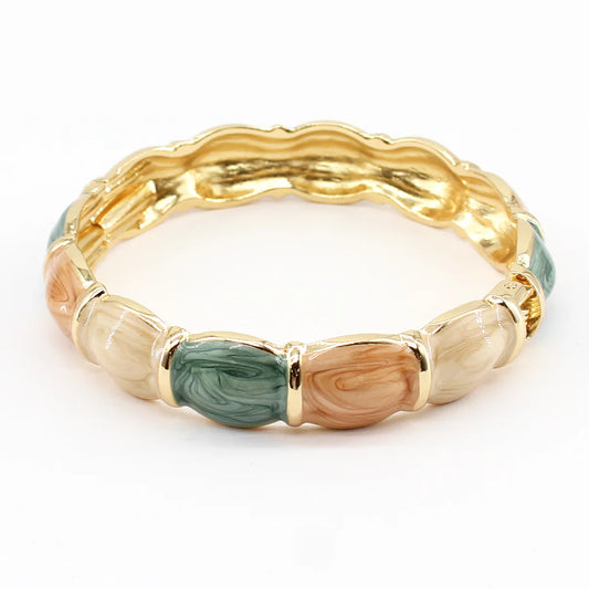 Gold bracelet with green and wood-like inlays on a white background