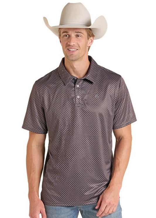 A man wearing a brown short-sleeve polo shirt with a small white geometric pattern, paired with a beige cowboy hat and blue jeans, against a plain white background.