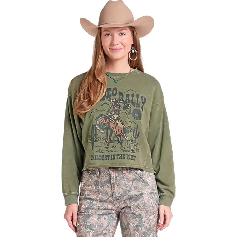 A woman wearing an olive green cropped sweatshirt with a vintage cowboy graphic, paired with camouflage pants and a tan cowboy hat, shown against a plain white background.