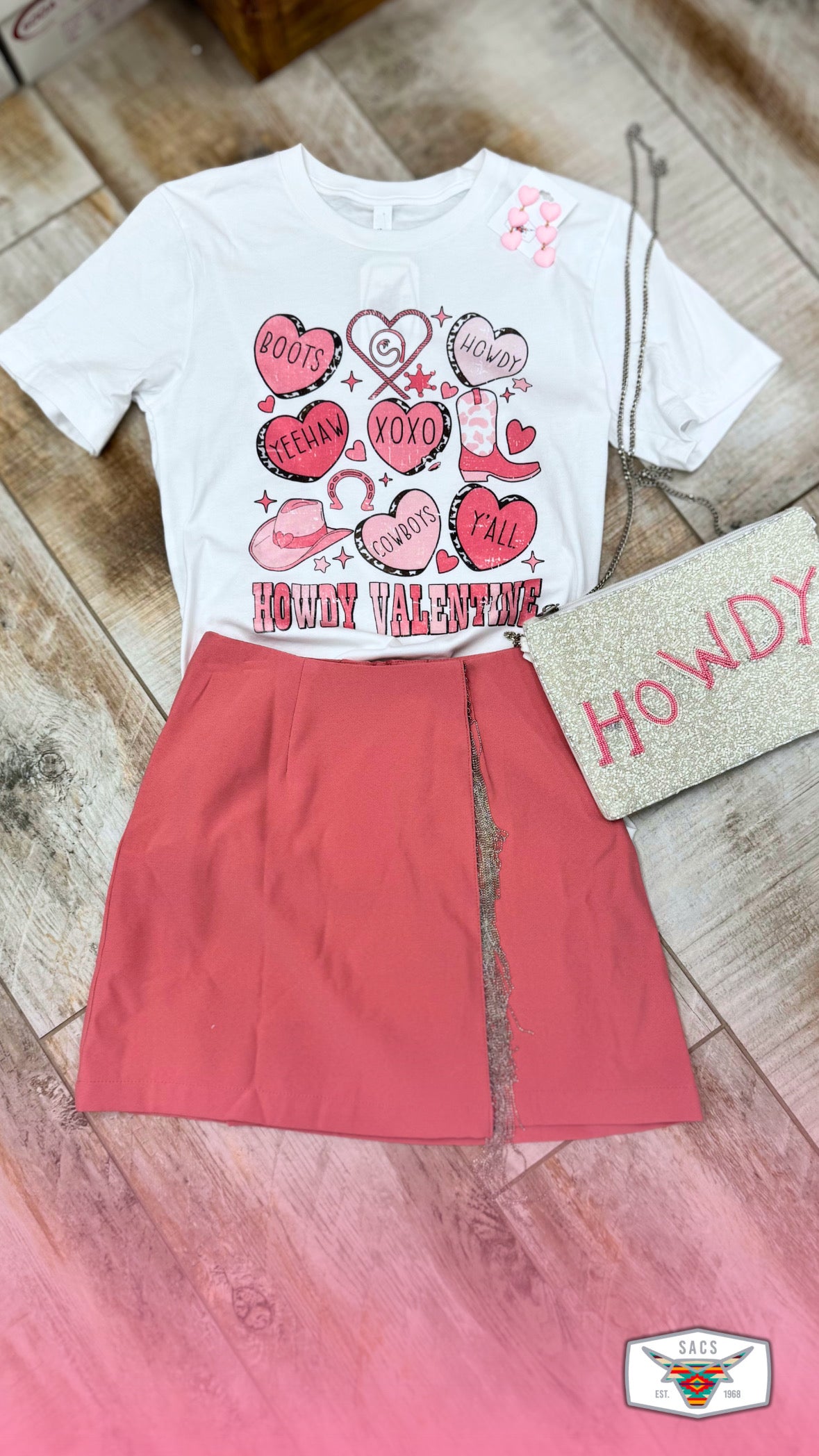Western Valentine graphic tee with red skirt and glitter HOWDY clutch on wood floor