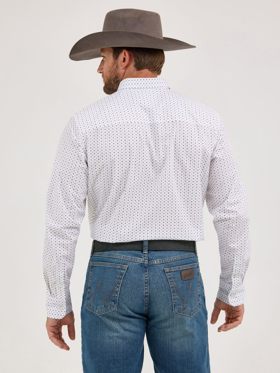 Man in grey cowboy hat, white patterned long sleeve shirt, and blue jeans, seen from behind.