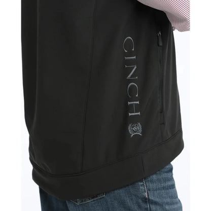 Person wearing a black Cinch vest over a striped shirt on a white background