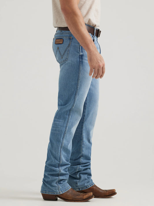Man wearing light blue bootcut jeans with brown belt and cowboy boots, side view