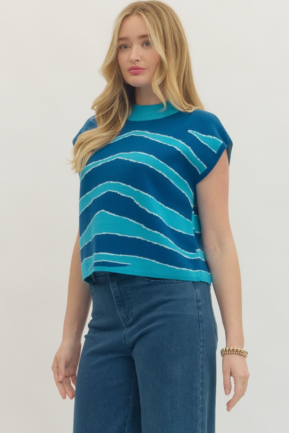 Woman wearing a blue and green striped shirt with high-waisted jeans on a plain background