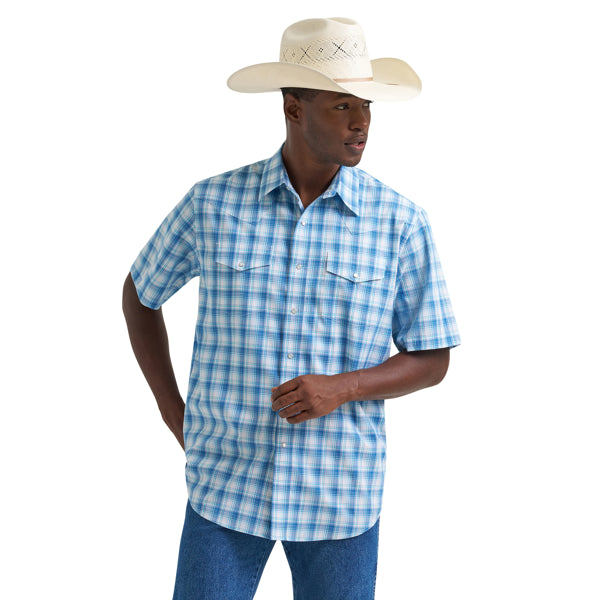 Man in a blue plaid short-sleeve western shirt, cowboy hat, and jeans, standing against white background.