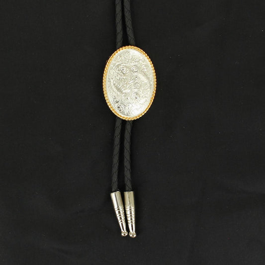 A western-style bolo tie featuring a black braided cord, a silver-toned engraved oval concho with a gold-toned border, and silver-toned metal tips, displayed on a black fabric background.