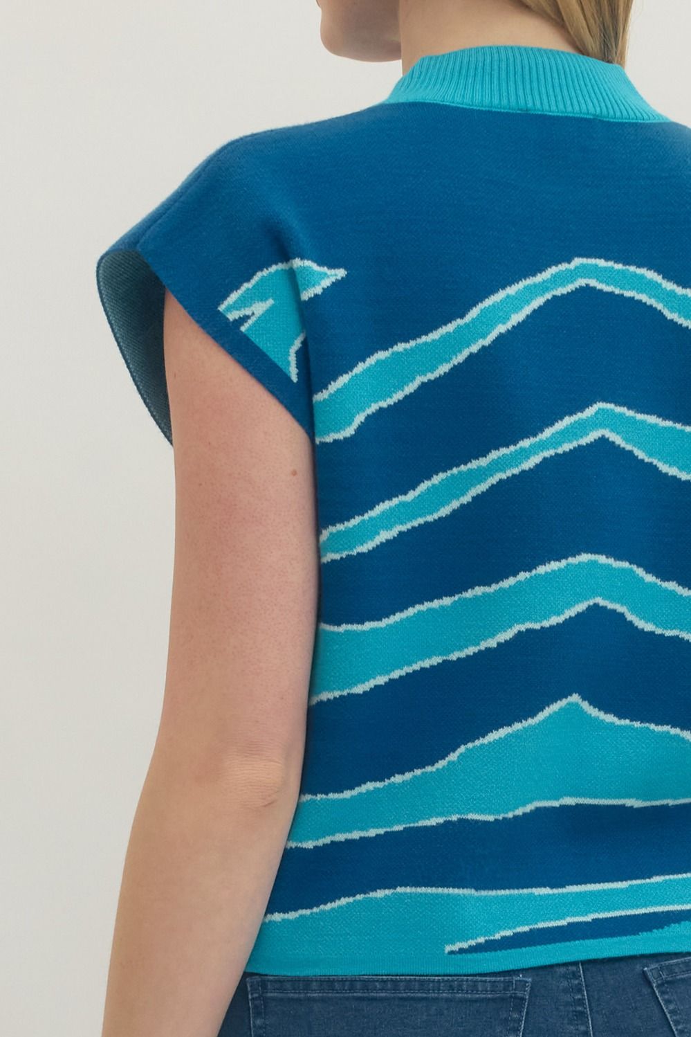 Blue sleeveless sweater with wave pattern worn by a person on a light background