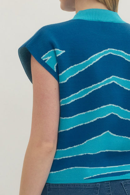 Blue sleeveless sweater with wave pattern worn by a person on a light background