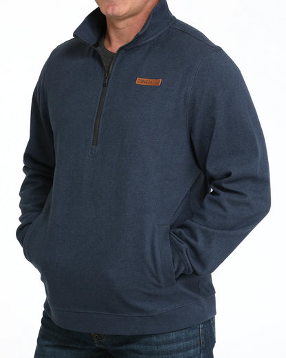 Man wearing navy blue quarter-zip pullover with pockets and brown logo patch on chest
