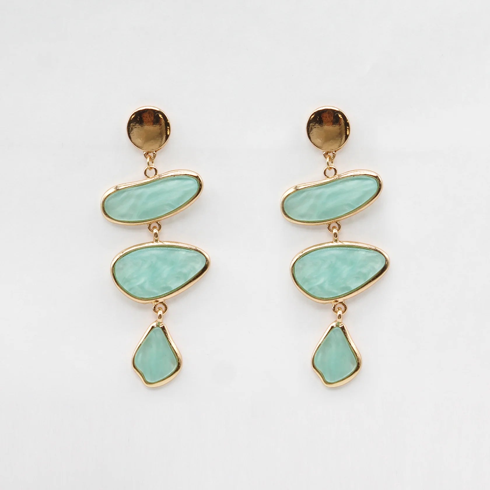 Pair of earrings with gold accents and turquoise stones on a light gray background