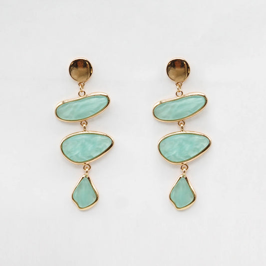 Pair of earrings with gold accents and turquoise stones on a light gray background