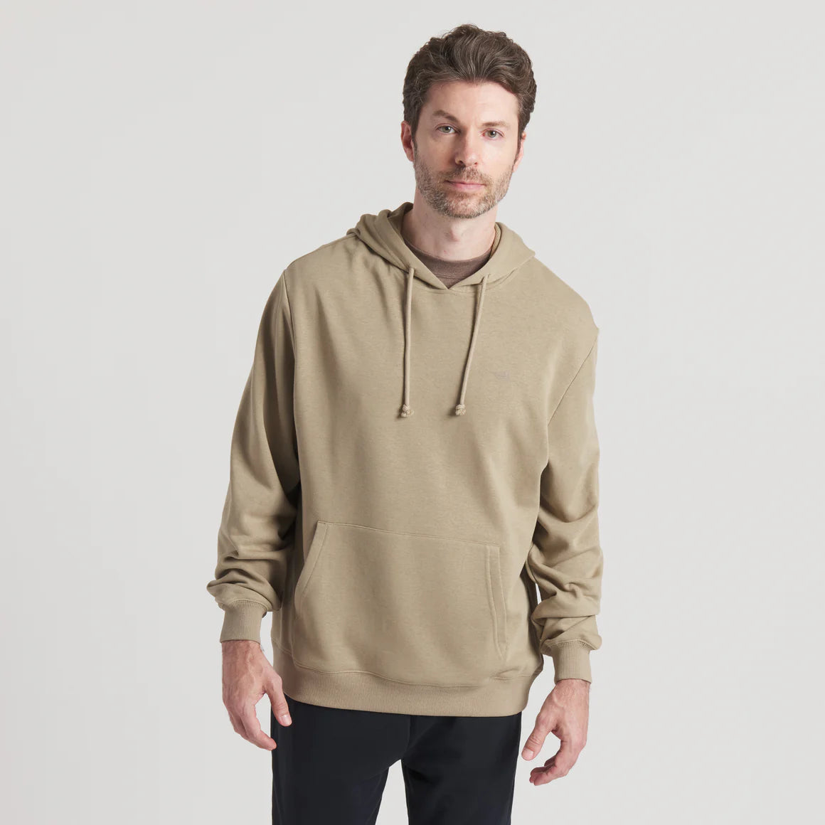 Man wearing a beige hooded sweatshirt with front pocket and drawstrings, casual outfit