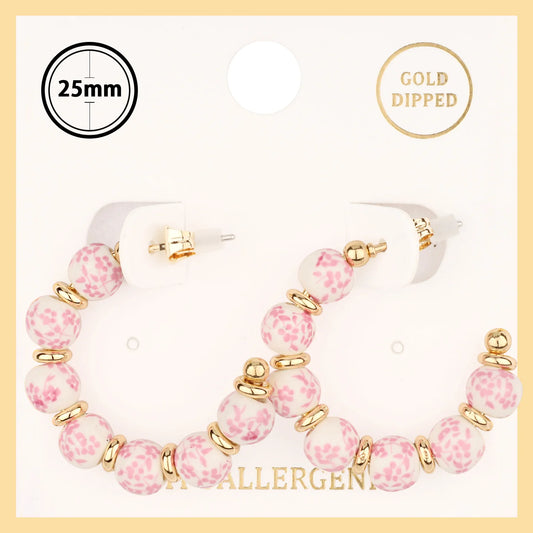 Pink beaded hoop earrings with gold accents on a beige background