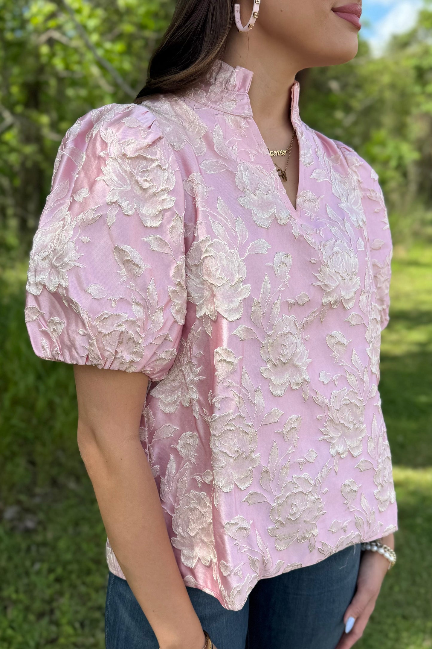Woman wearing a pink floral blouse outdoors with greenery in the background