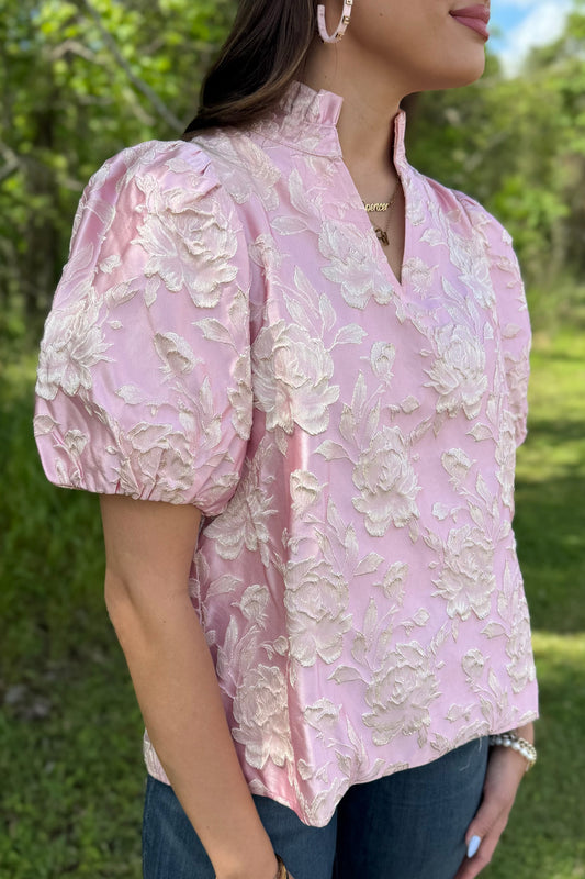 Woman wearing a pink floral blouse outdoors with greenery in the background