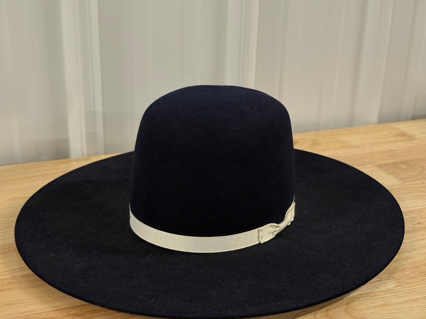 Wide brim black felt hat with cream ribbon on wooden table