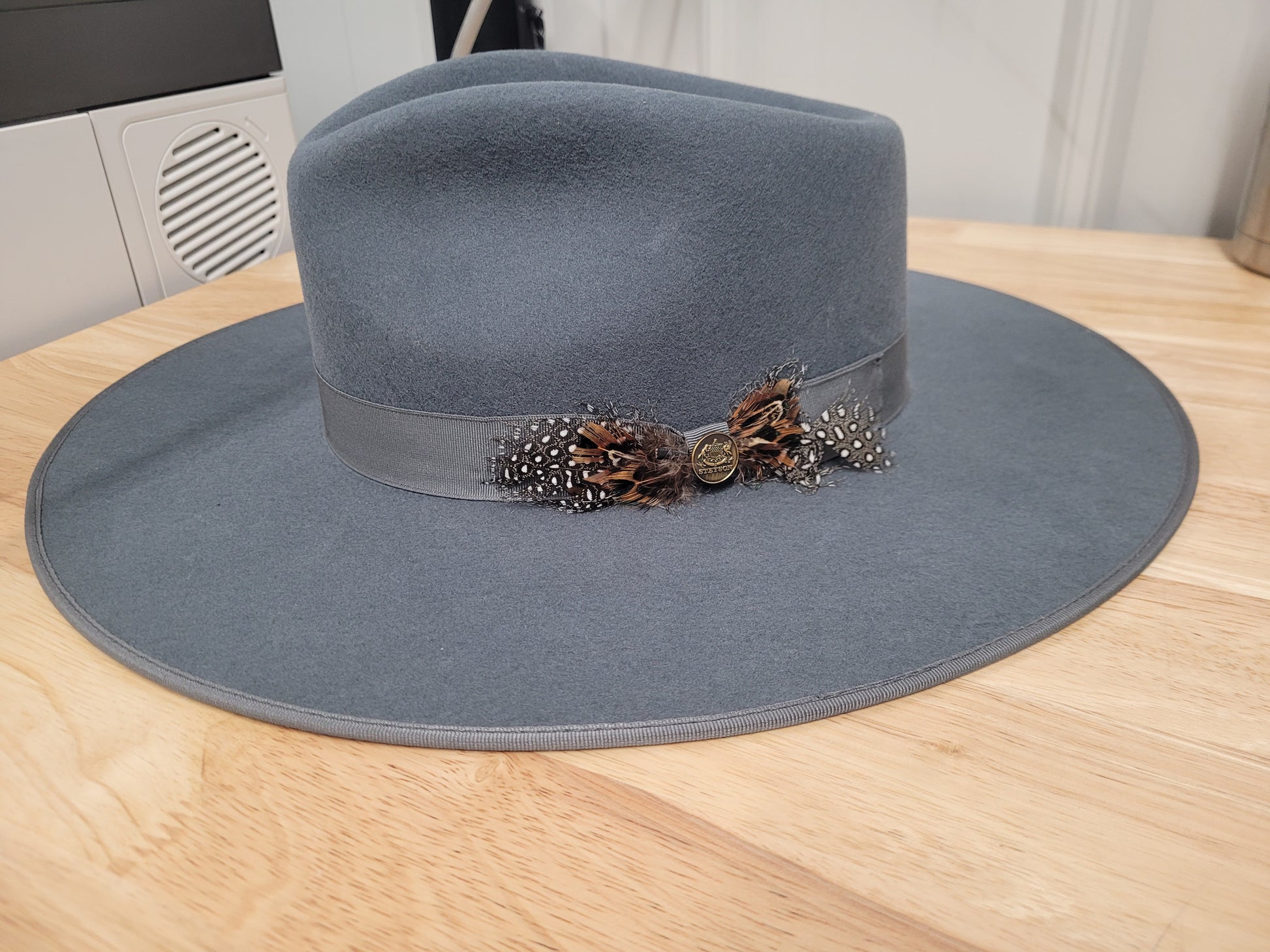 Gray wide brim felt hat with ribbon band and feather accent on wooden table