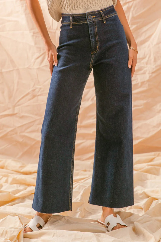 Woman wearing high waisted wide leg dark blue jeans and white sandals