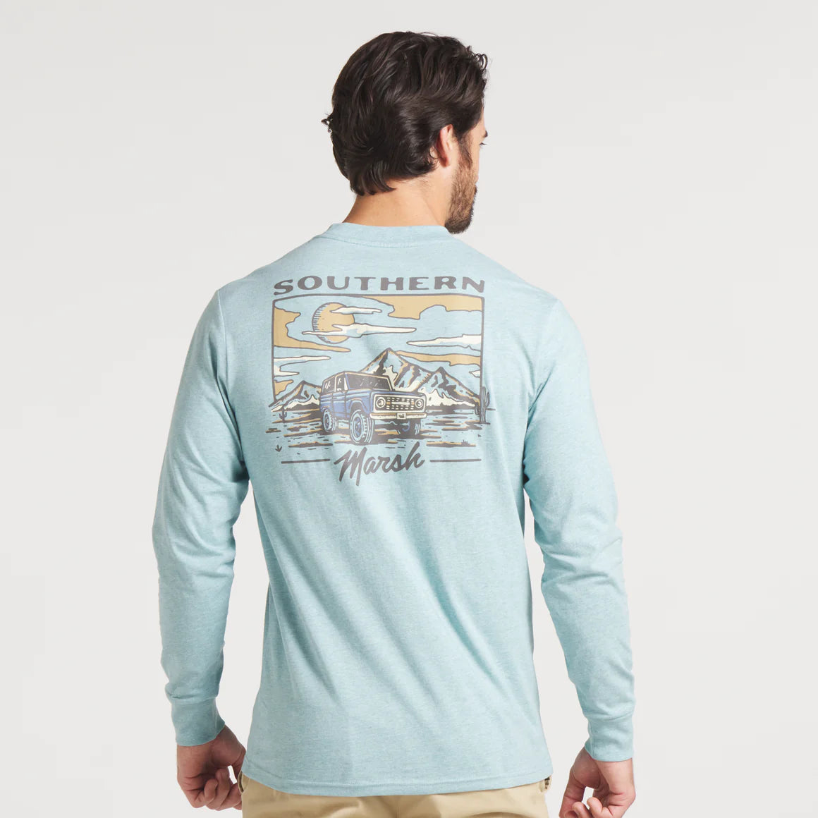 Man wearing light blue long sleeve shirt with Southern Marsh graphic, mountains and SUV illustration