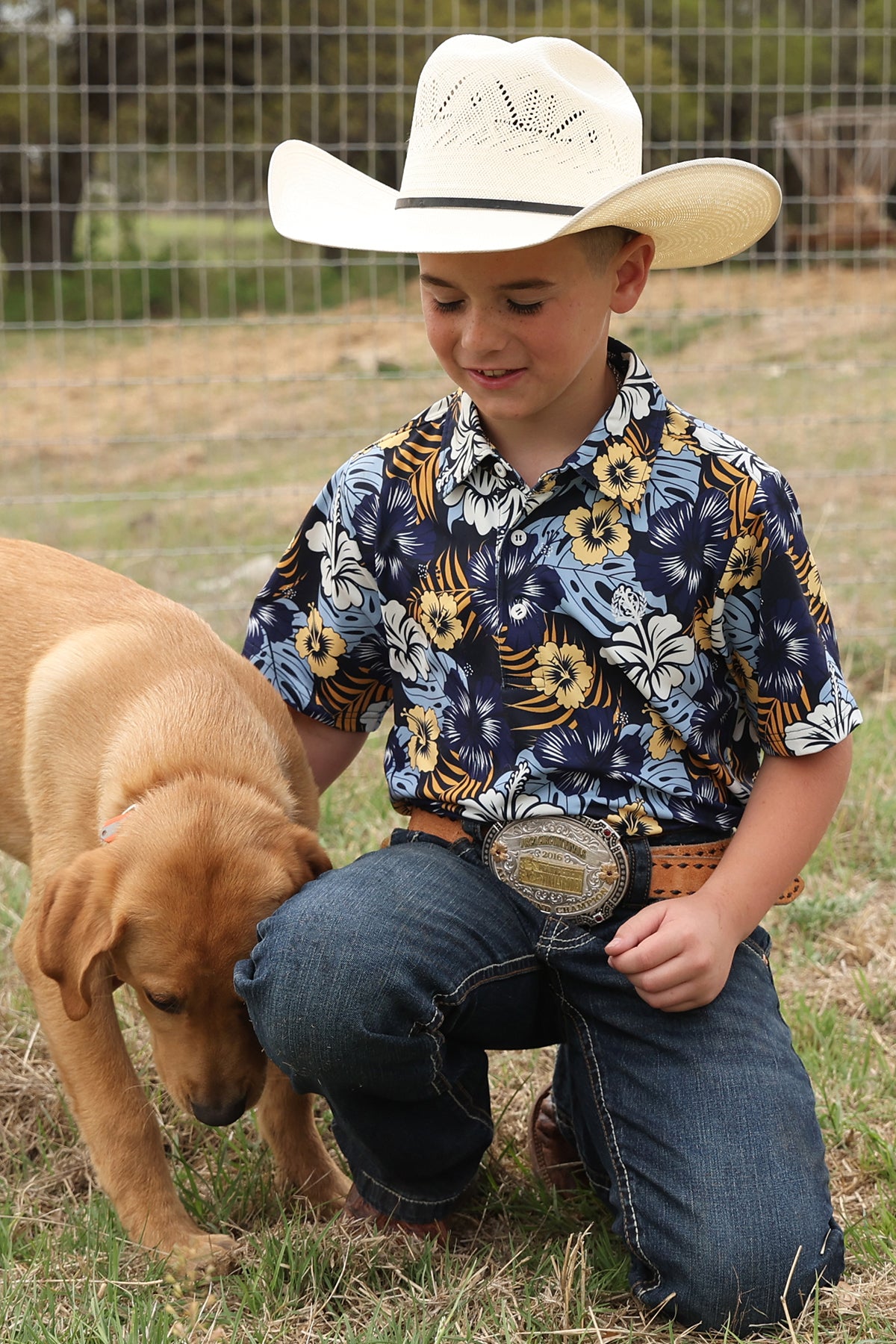 Child in cowboy hat and floral shirt with a dog outdoors