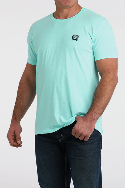 Man wearing light blue short sleeve t-shirt with small chest logo and dark jeans