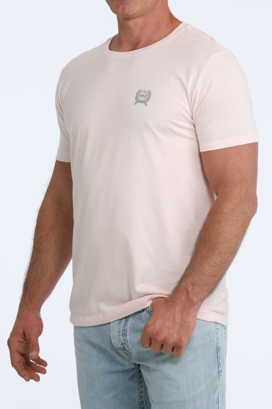 Man wearing a beige t-shirt with a small logo on a white background