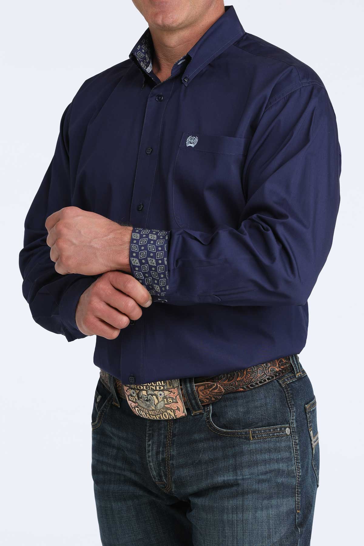 Person wearing a navy blue shirt with a patterned cuff and jeans on a white background