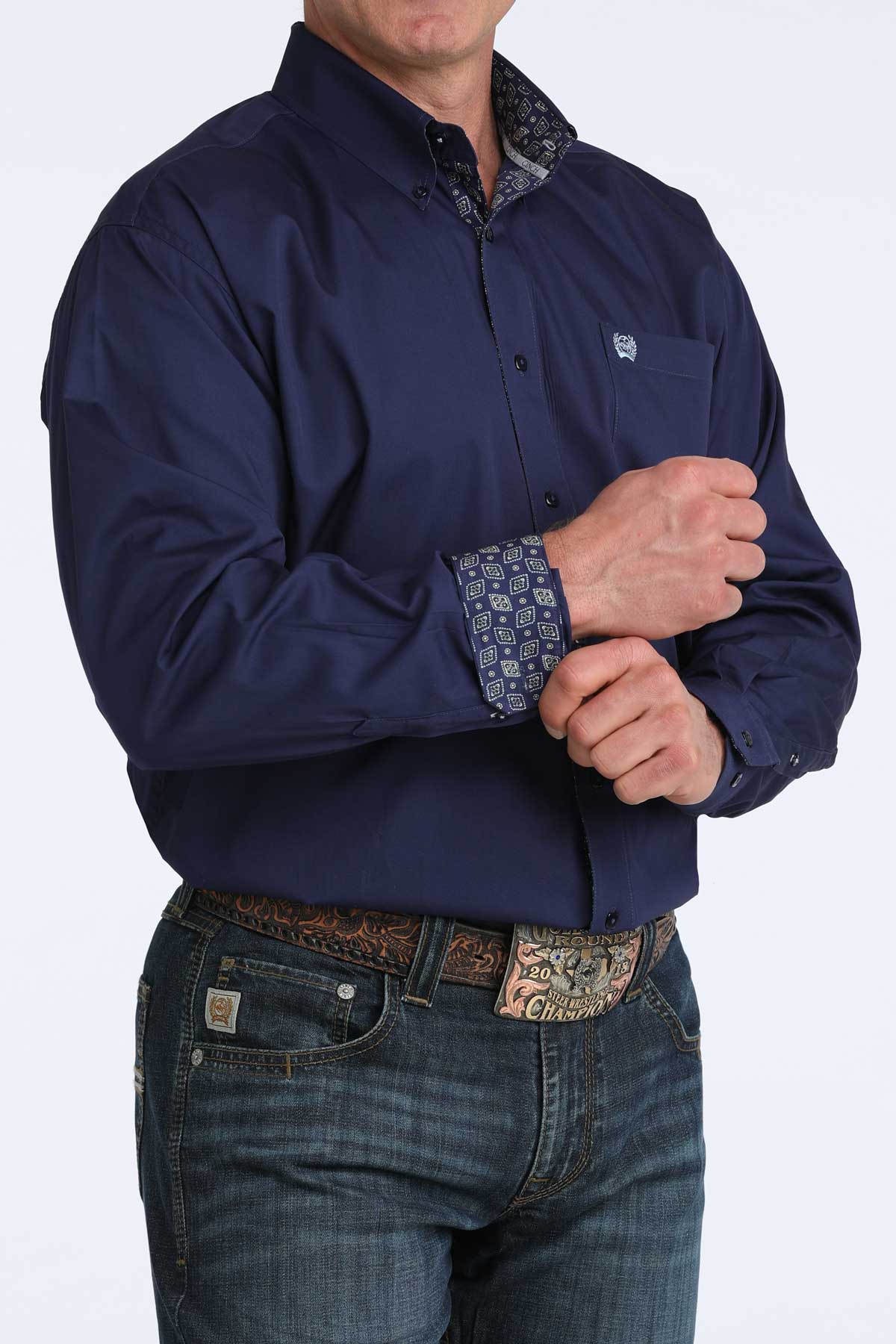 Man wearing a navy blue shirt with patterned cuffs and jeans on a white background