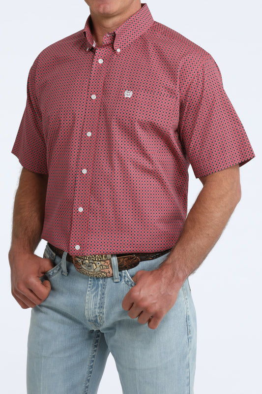 Man wearing a red patterned shirt and light blue jeans on a white background