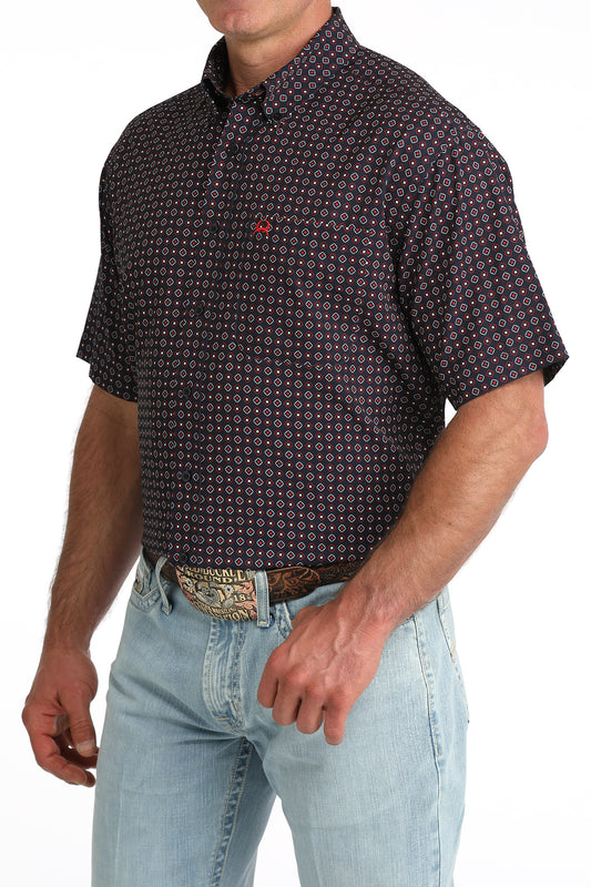 Man wearing a patterned short-sleeve shirt and light blue jeans on a white background