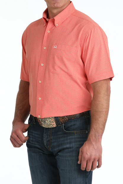 Man wearing a coral patterned short-sleeve shirt and blue jeans on a white background