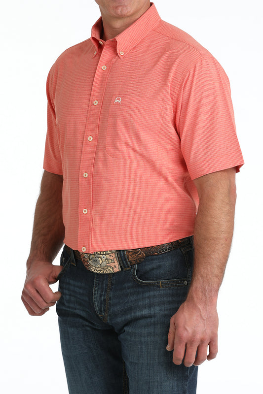 Man wearing a coral patterned short-sleeve shirt and blue jeans on a white background
