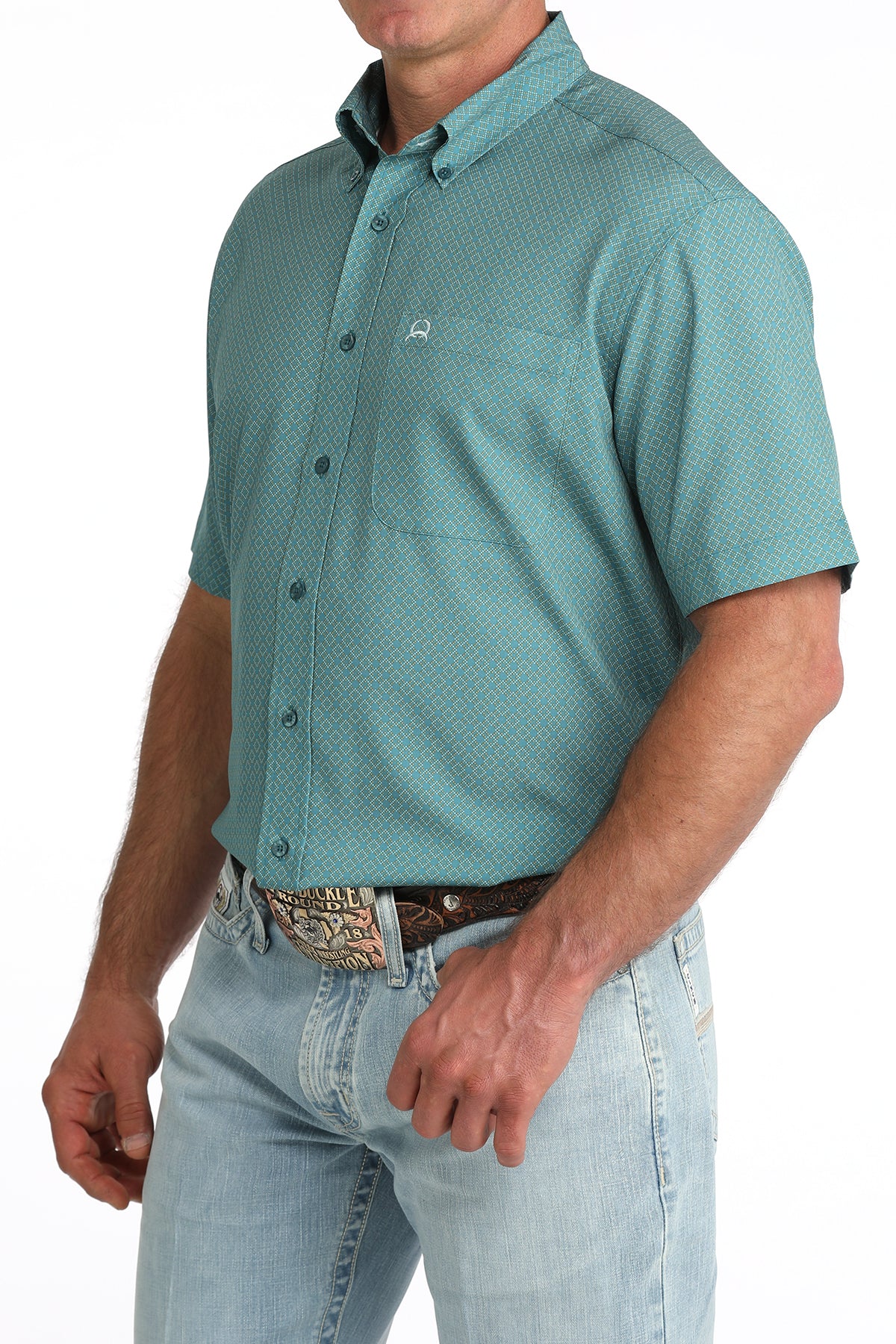 Man wearing a teal patterned shirt and light blue jeans on a white background