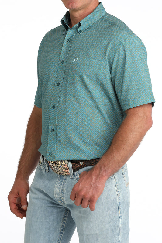 Man wearing a teal patterned shirt and light blue jeans on a white background