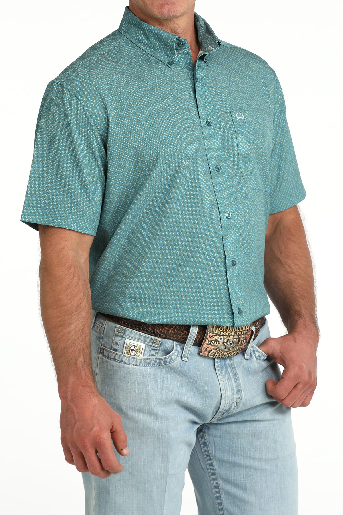 Man wearing a teal patterned button-up shirt and light blue jeans on a white background