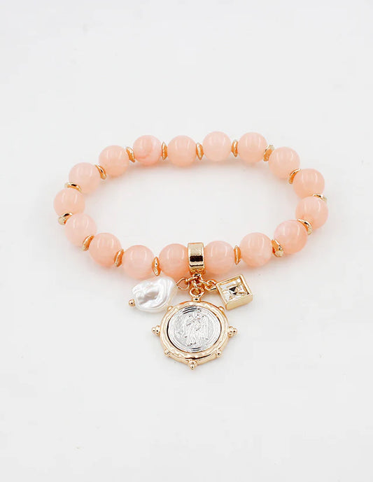 Pink beaded bracelet with gold accents and charms on a white background