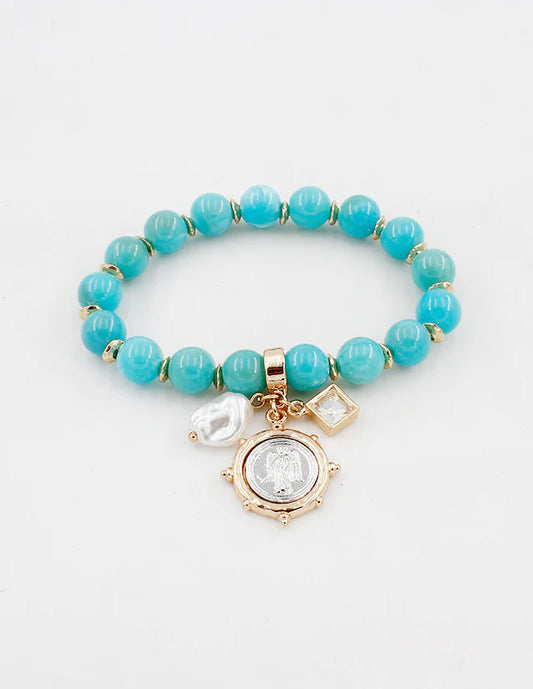 Turquoise beaded bracelet with gold charm on a light gray background