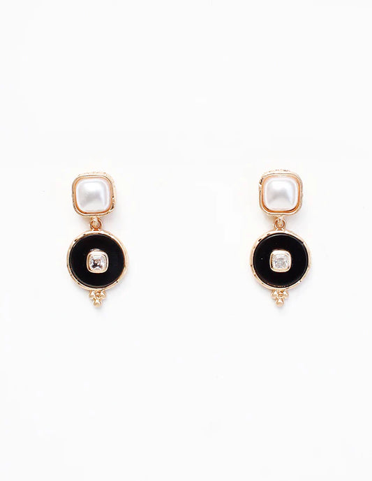 Pair of earrings with black circular designs and pearl-like centers on a white background
