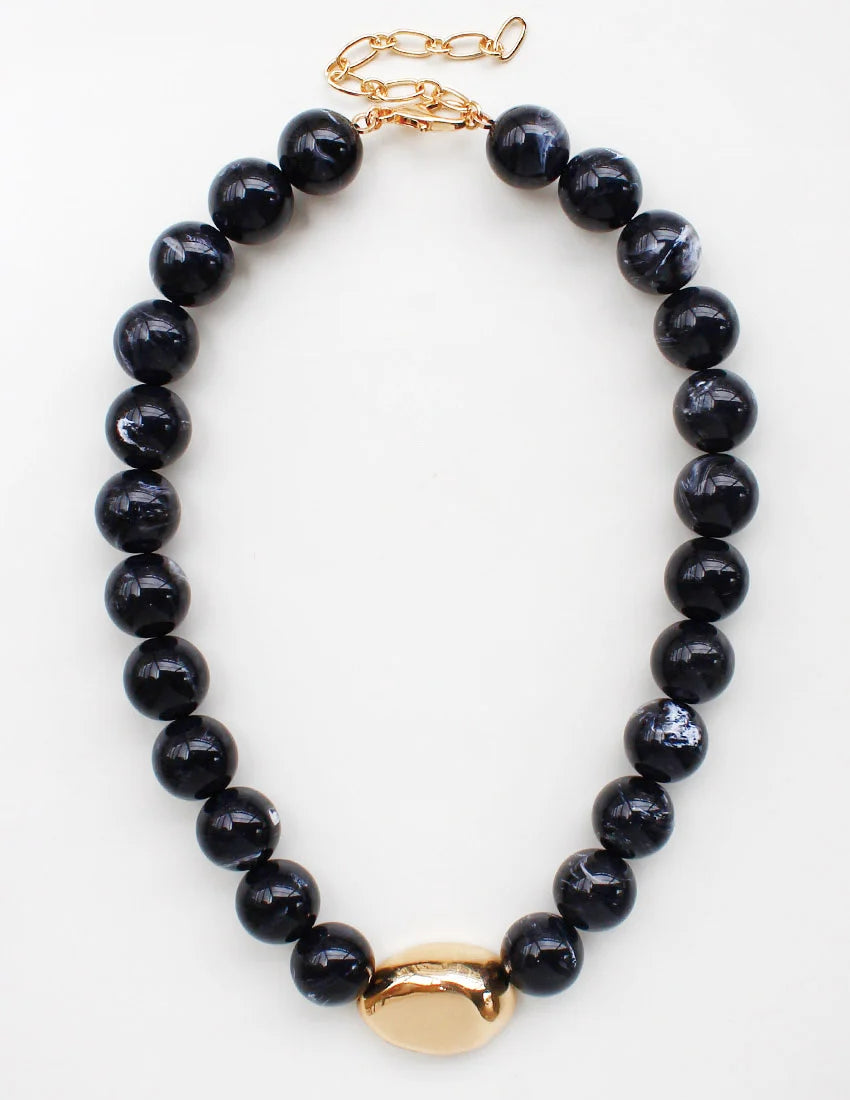 A beaded necklace featuring glossy black round beads and a polished gold-tone oval centerpiece, displayed on a clean white background.
