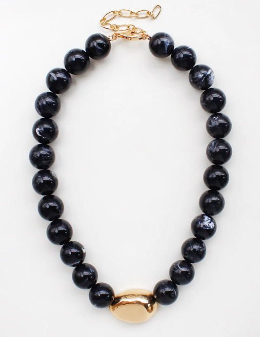 A beaded necklace featuring glossy black round beads and a polished gold-tone oval centerpiece, displayed on a clean white background.