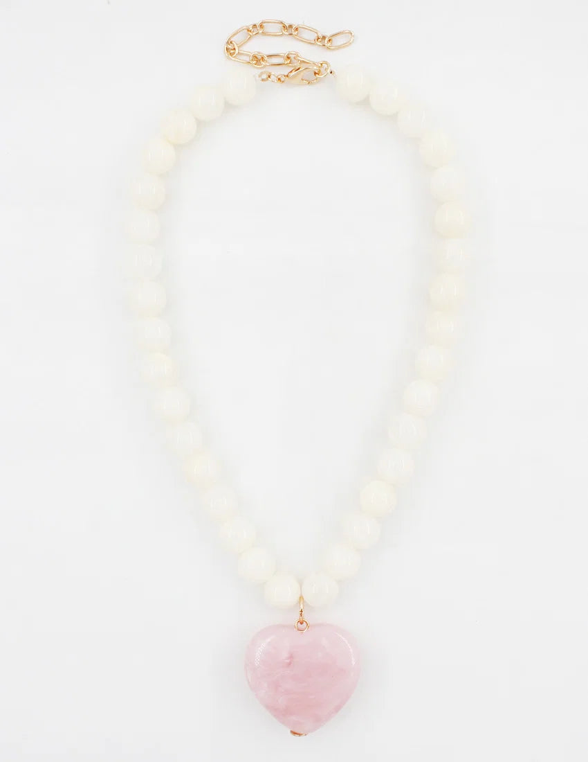 A beaded necklace featuring a strand of matte white round beads with a polished pink heart-shaped stone pendant, finished with a gold-tone clasp.