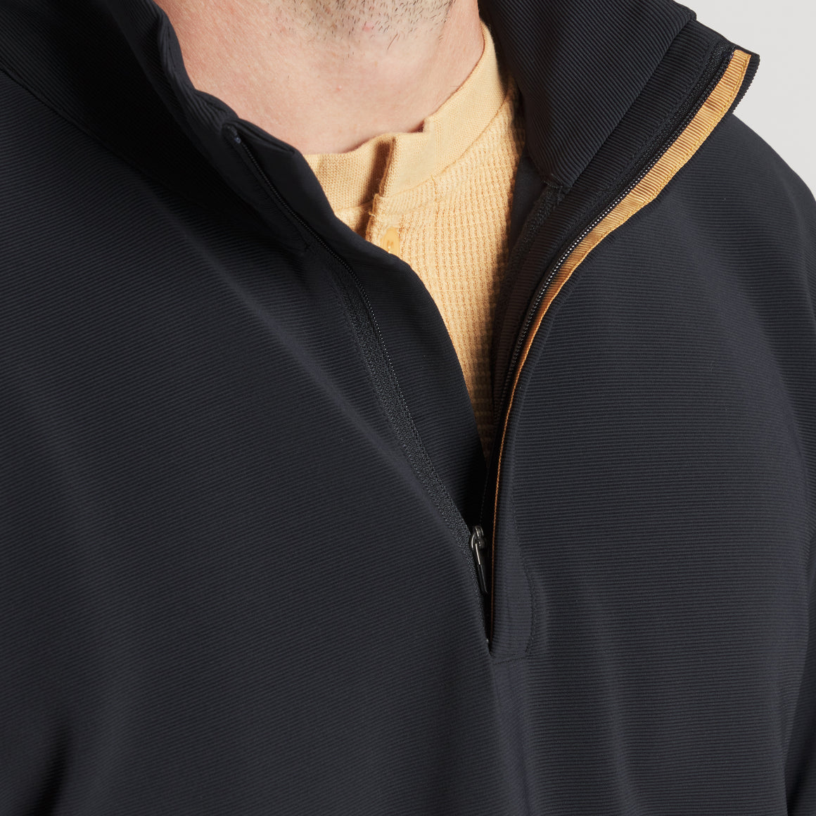 Close-up of a black zip-up jacket with a high collar, layered over a beige waffle-knit shirt
