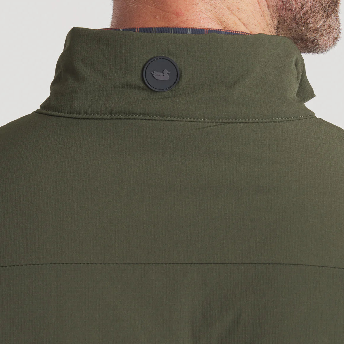 Close-up of olive green jacket collar with rubber duck logo patch detail