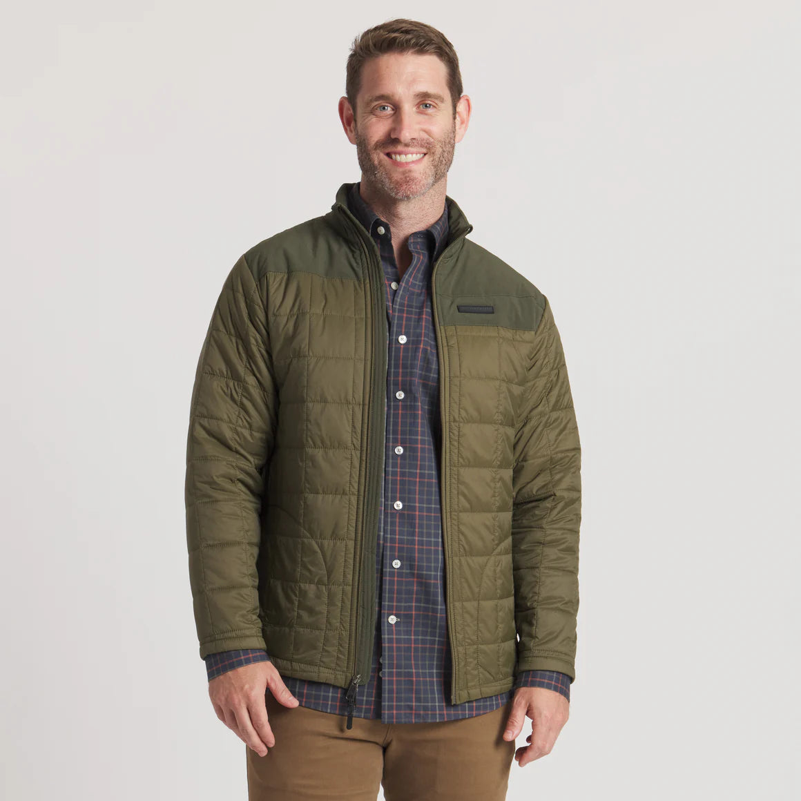Man wearing olive green quilted jacket over plaid shirt, outdoor casual style